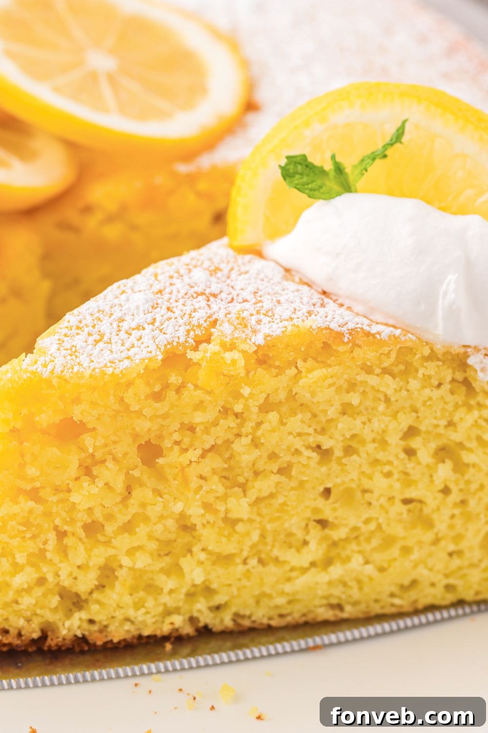 close up of Italian Lemon Ricotta Cake on plate with lemons sliced behind it on table 