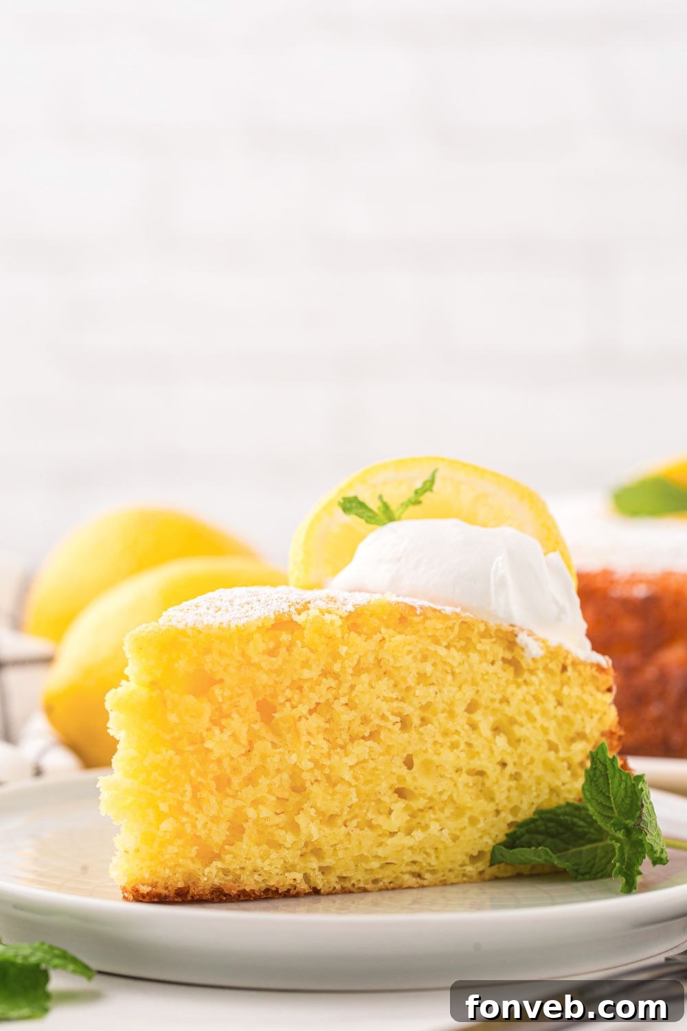 side view of table with a slice of Italian Lemon Ricotta Cake on plate with mint leaf to side of plate 