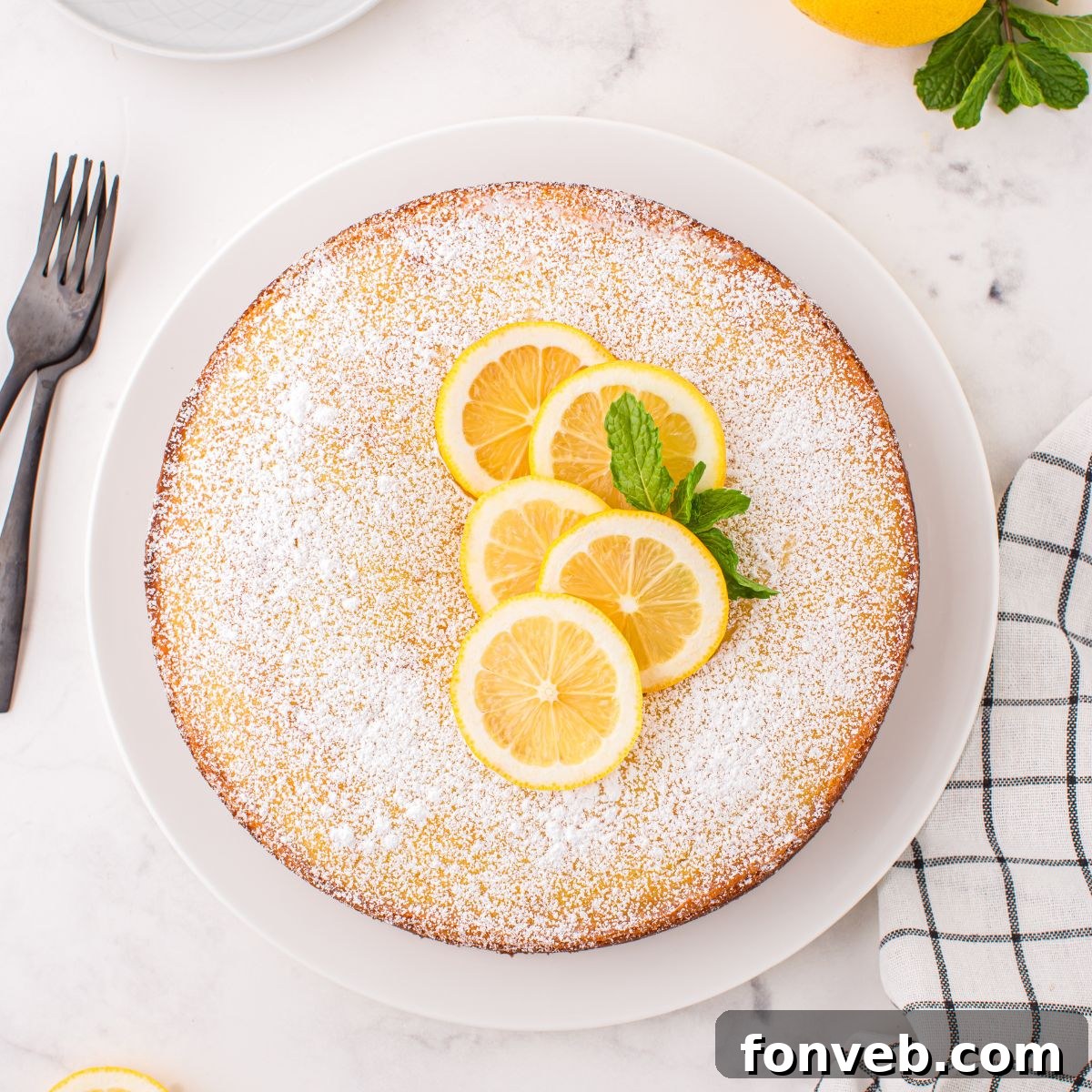 Italian Lemon Ricotta Cake on table with some fresh lemons on top with some mint leaves to side 