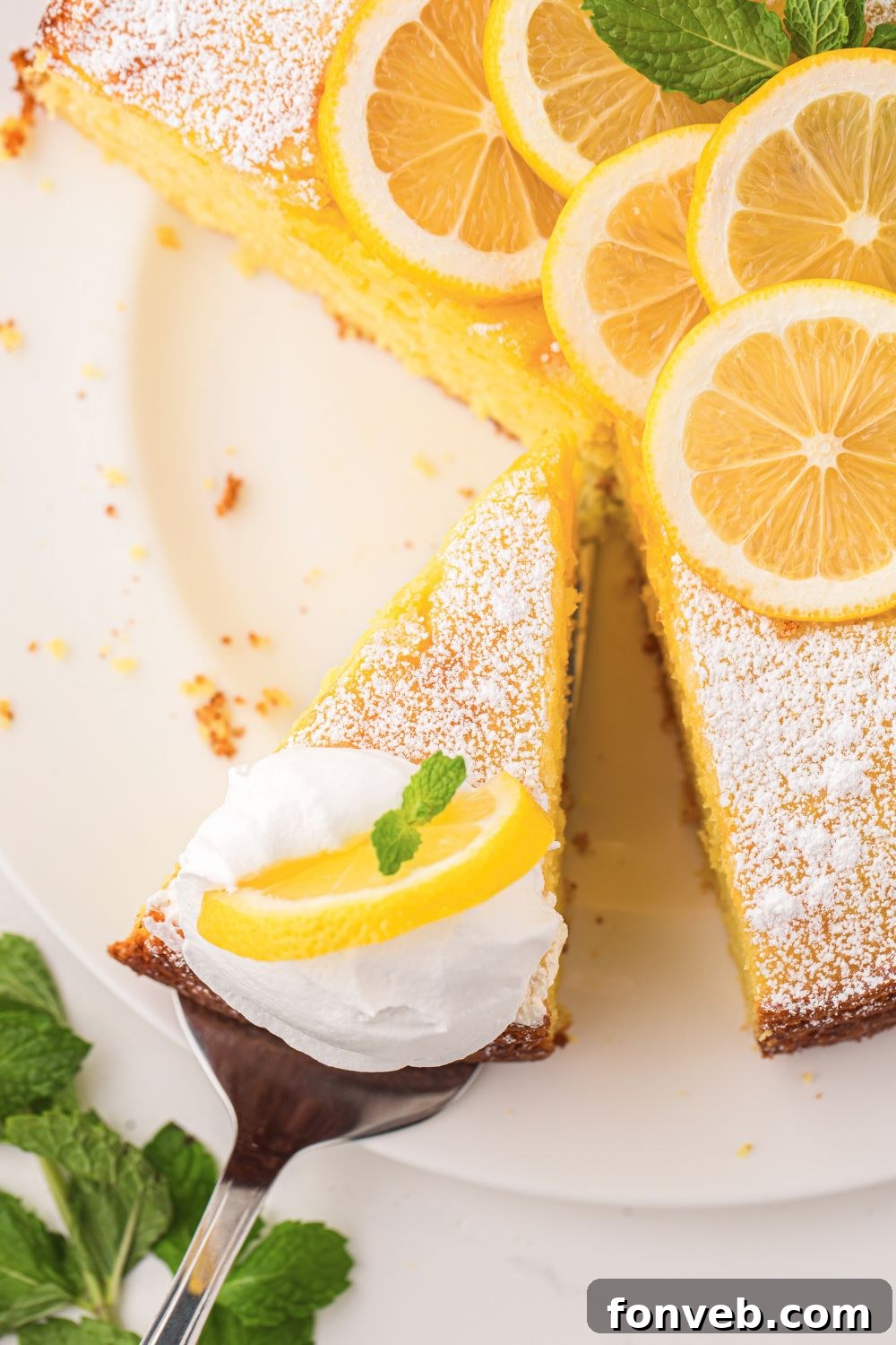 Italian Lemon Ricotta Cake being lifted off the cake platter with more sitting on table 