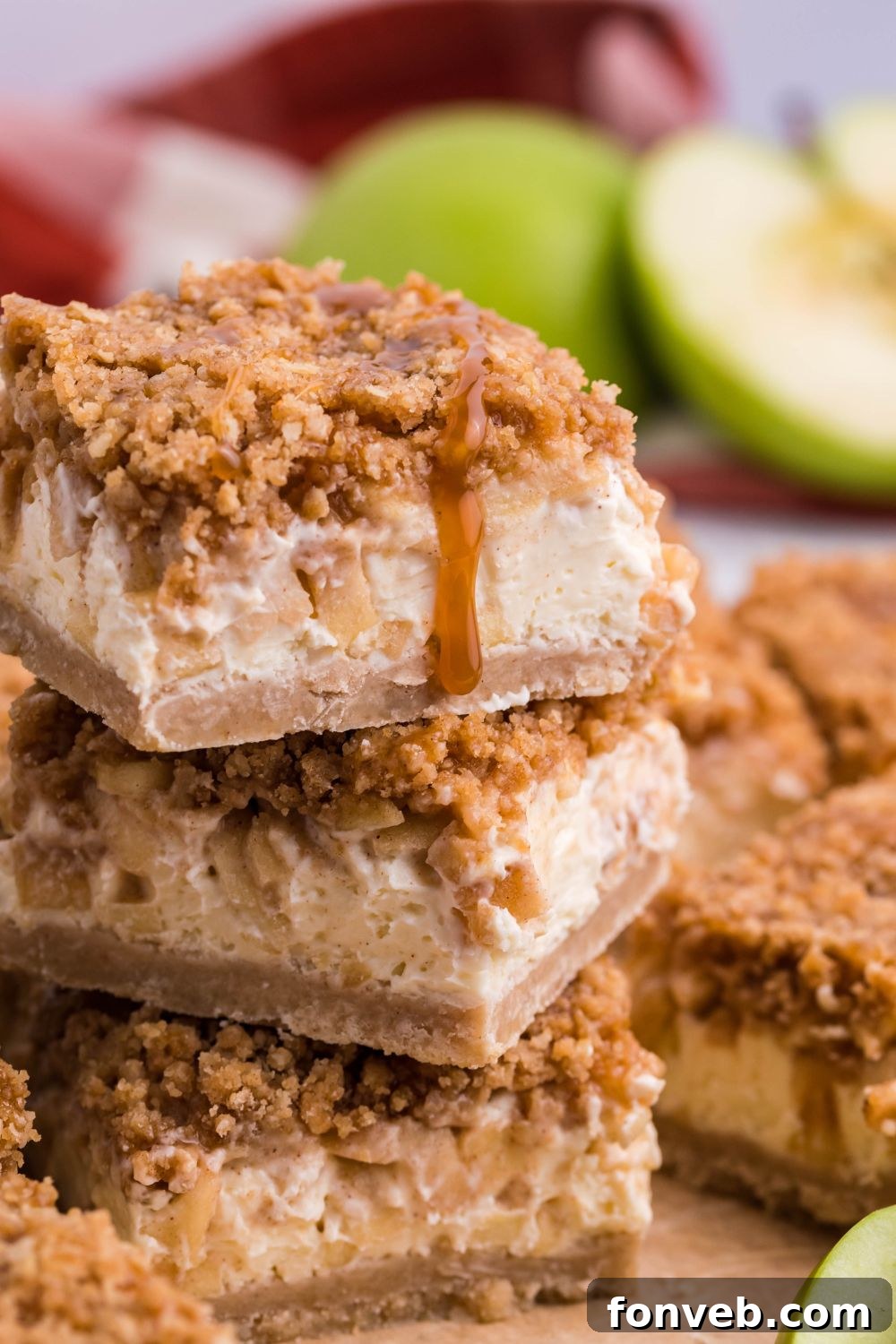 Caramel Apple Cheesecake Bars stacked on top of one another on table with apple sliced in half to side 