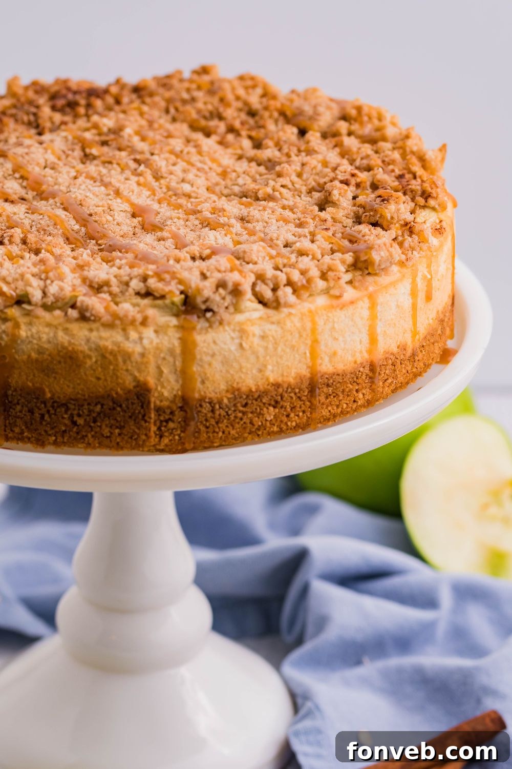 Decadent Caramel Apple Crumble Cheesecake 12 A full Caramel Apple Crisp Cheesecake presented on a pie plate, accompanied by a few fresh green apples to the side, emphasizing its fresh, fruity appeal.