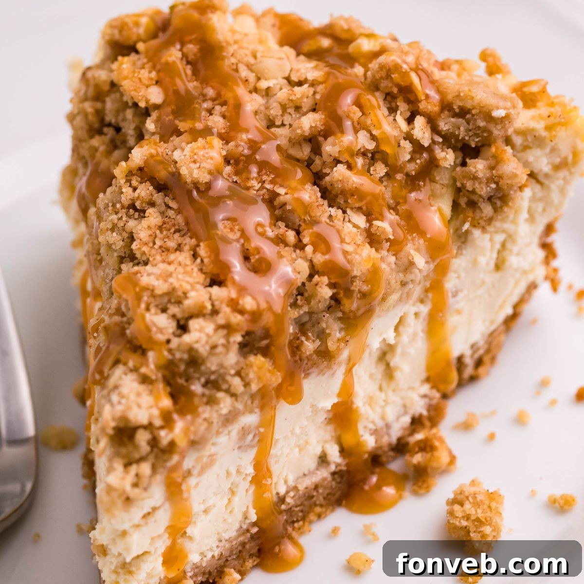 Decadent Caramel Apple Crumble Cheesecake 3 A delectable slice of Caramel Apple Crisp Cheesecake elegantly presented on a plate with a fork poised to the side, showcasing its perfectly baked layers and golden-brown crumble.