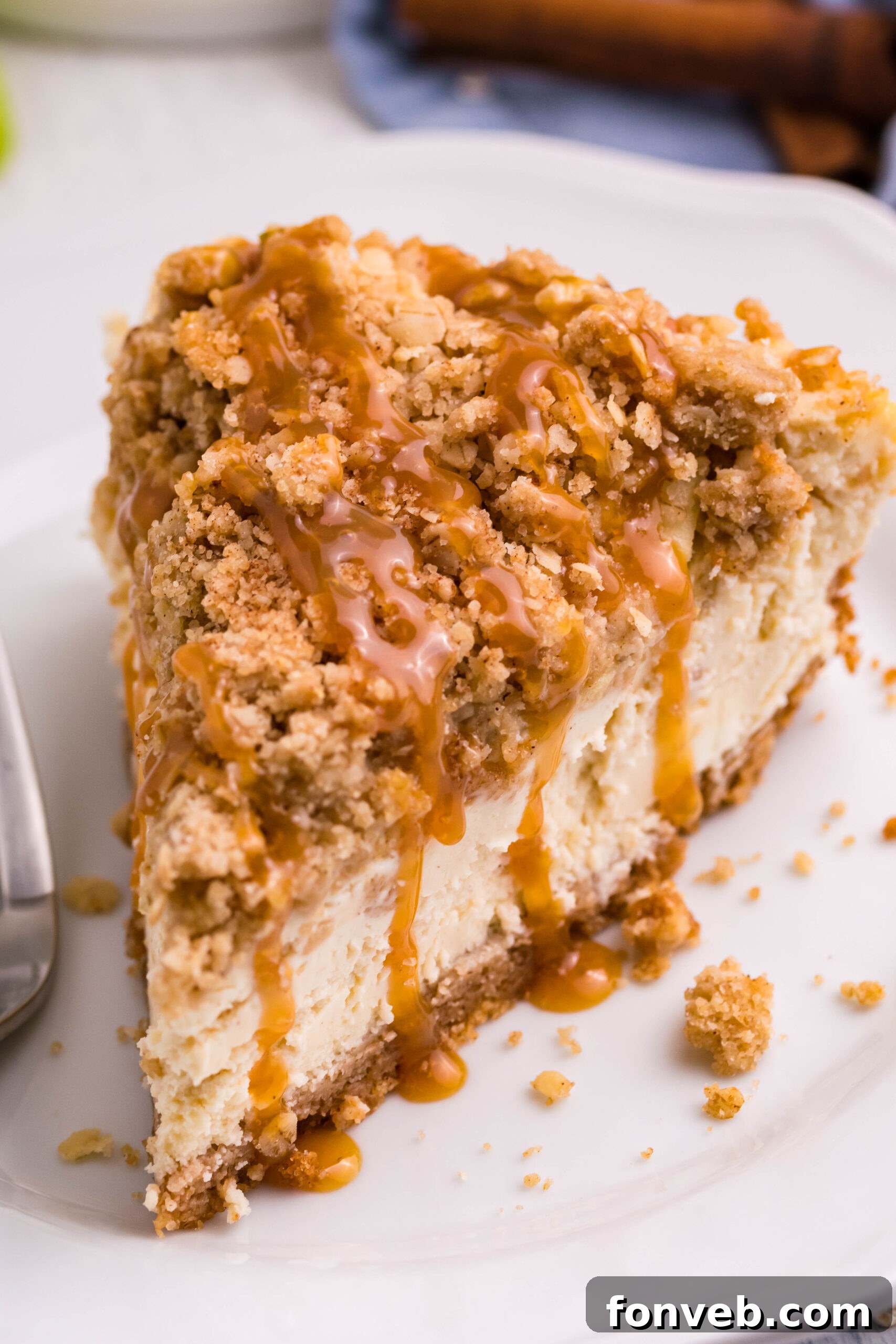 Decadent Caramel Apple Crumble Cheesecake 4 An overhead shot of a single slice of Caramel Apple Crisp Cheesecake on a pristine white plate, highlighting the distinct layers of crust, creamy filling, spiced apples, and oat crumble, all glistening with caramel.