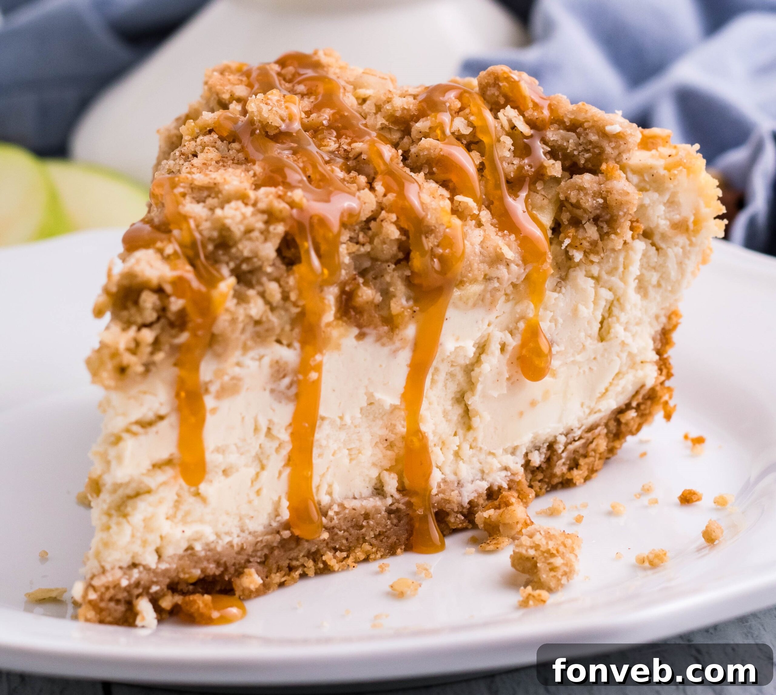 Decadent Caramel Apple Crumble Cheesecake 6 A beautifully presented slice of Caramel Apple Crisp Cheesecake, generously drizzled with golden caramel, resting on a white plate. The intricate layers are visible and inviting.