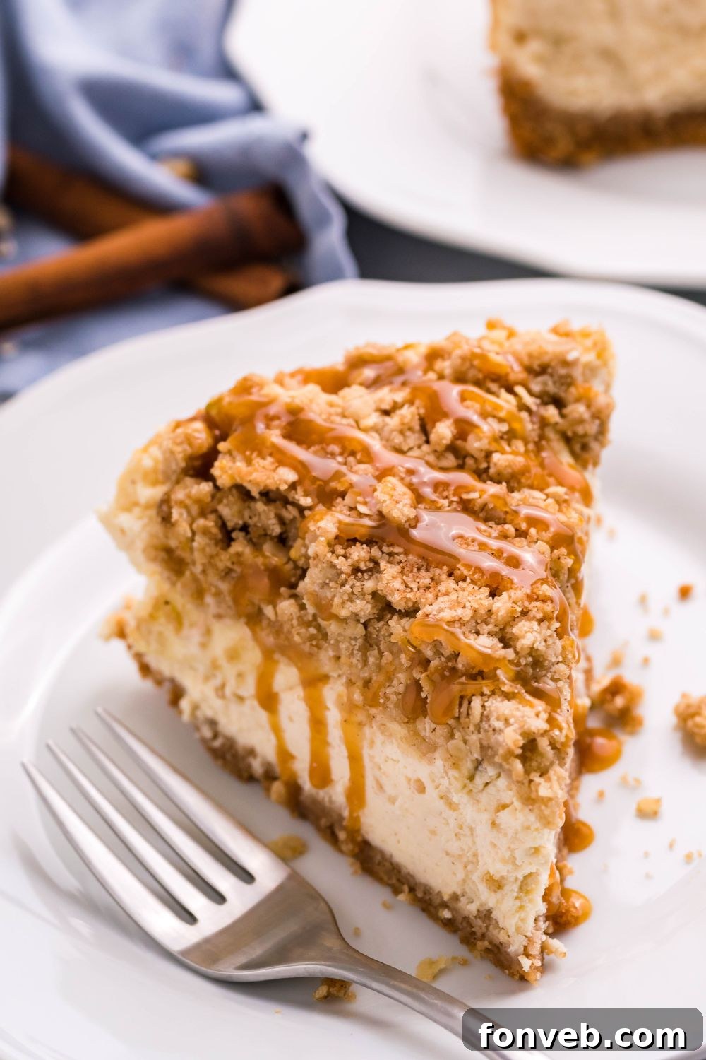 Decadent Caramel Apple Crumble Cheesecake 10 A slice of Caramel Apple Crisp Cheesecake on a plate with a fork beside it, inviting a taste.