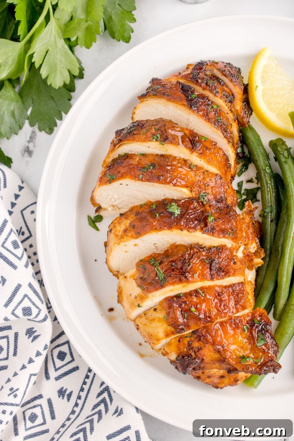 Air Fryer Chicken Breast sliced on plate with some green beans and lemon wedge to side on plate 