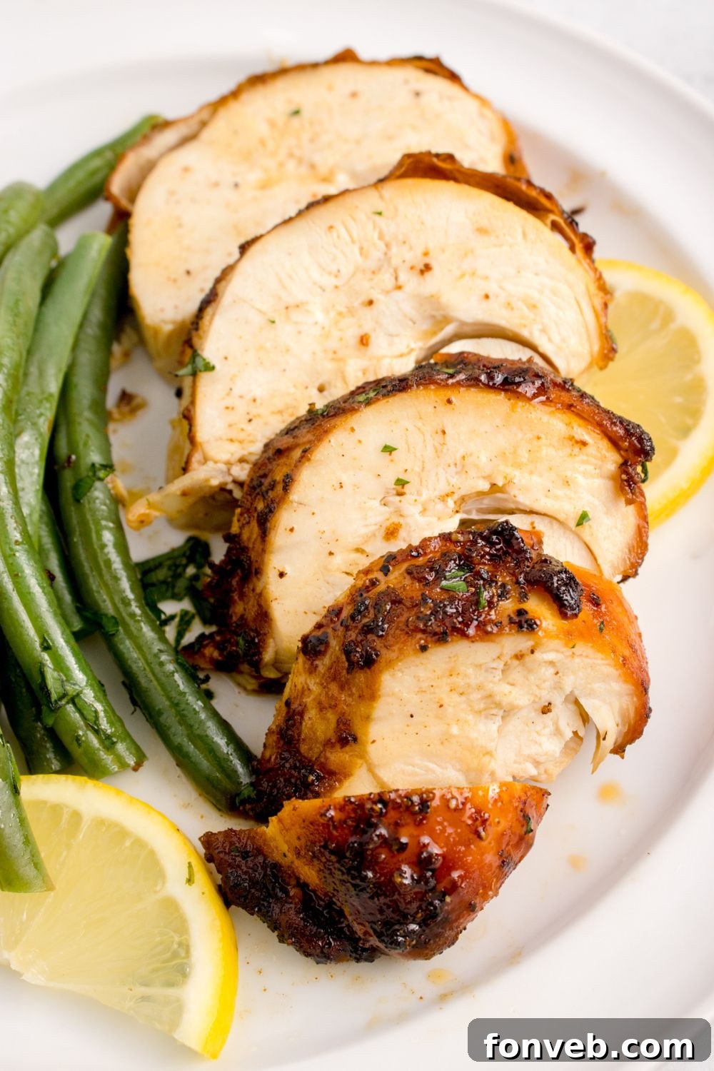 sliced Air Fryer Chicken Breast into strips on plate with green beans and lemon wedges to the side 