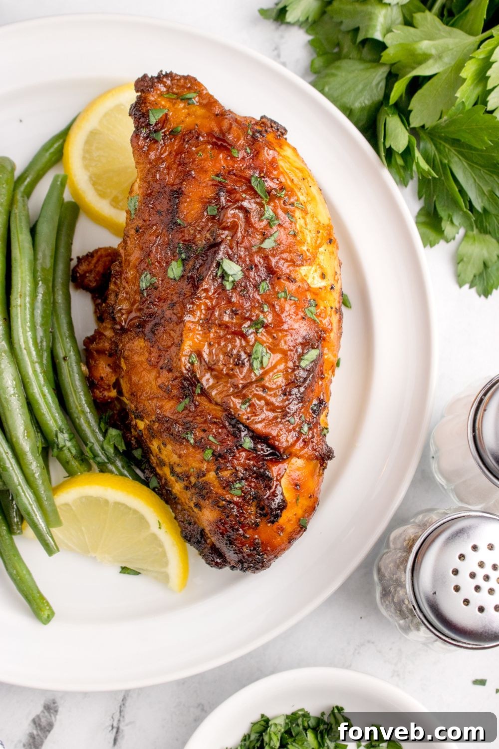 overhead look at table with Air Fryer Chicken Breast on plate withs some green beans, parsley, and salt and pepper to the side 