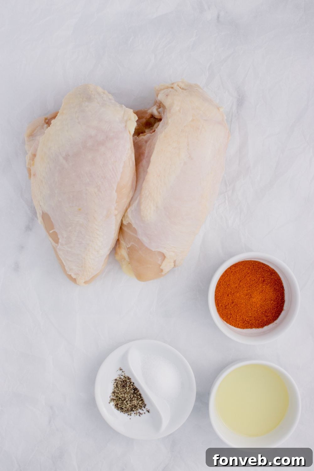 Air Fryer Chicken Breast ingredients on table, chicken breasts, seasonings in bowls, and oil in a small bowl 