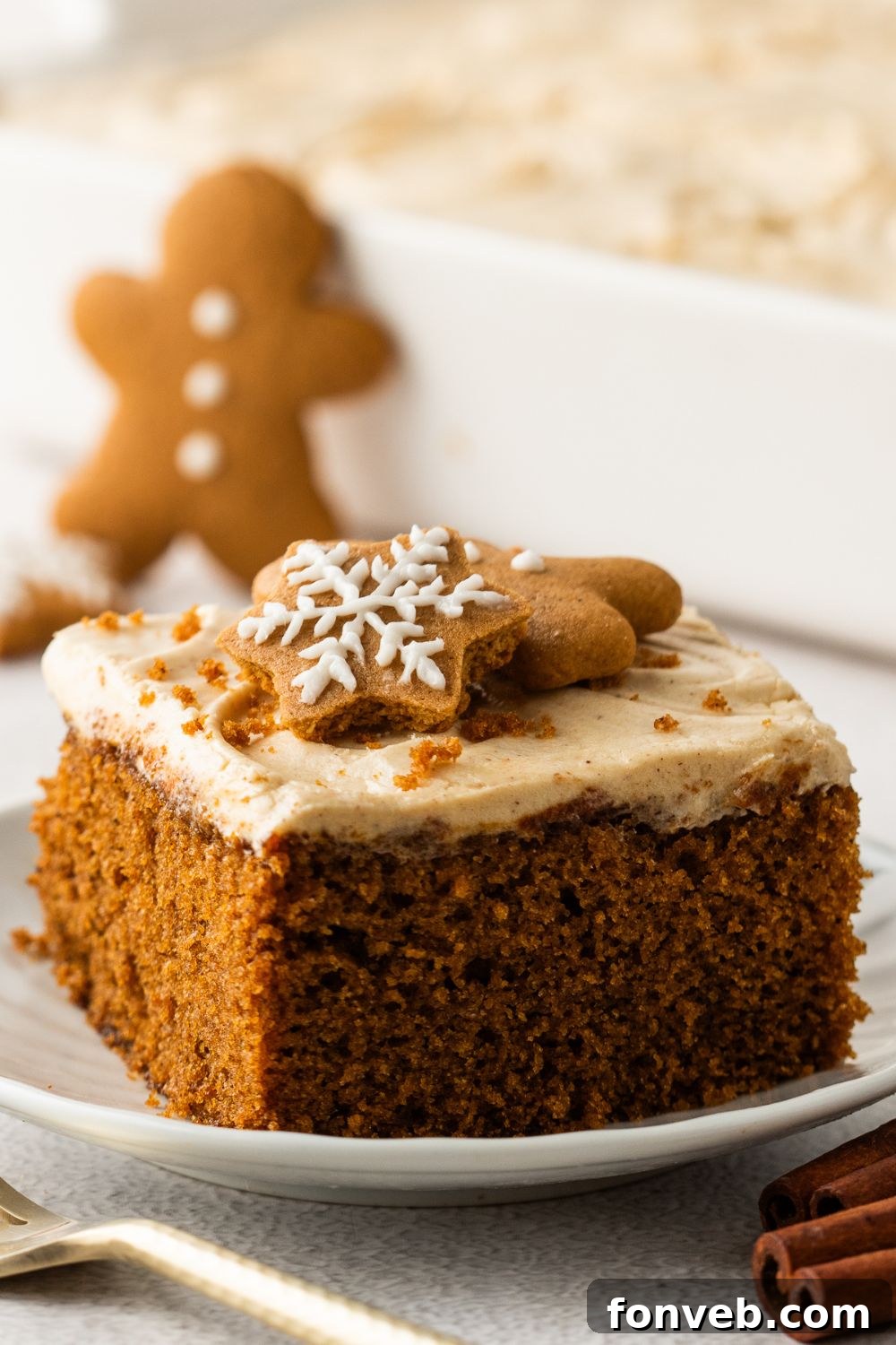slice of Gingerbread Cake with Cream Cheese Frosting on plate with a gingerbread cookie behind plate