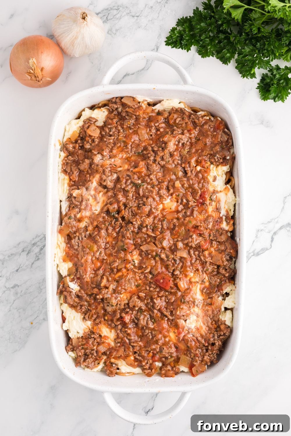 Creamy cheese mixture being carefully spread over the spaghetti layer in the baking pan