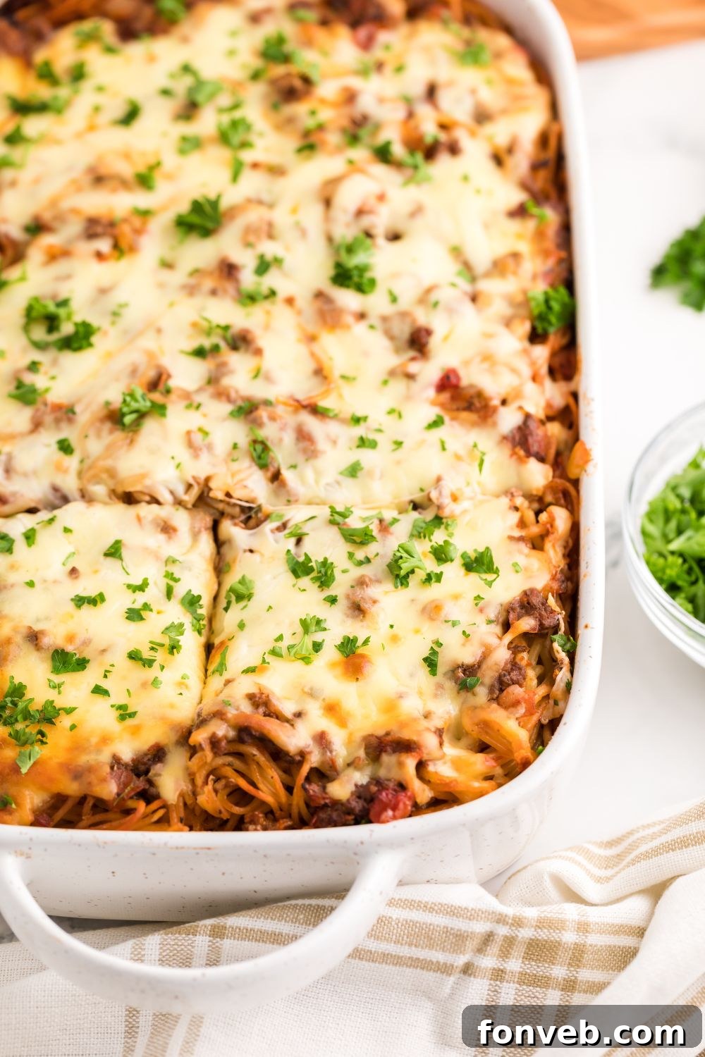 Million Dollar Spaghetti Casserole in a pan, garnished with fresh parsley and precisely cut into perfect squares for serving