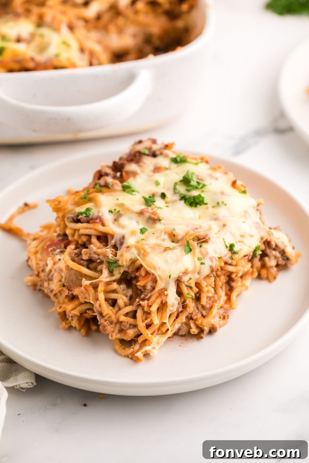 A neatly sliced portion of Million Dollar Spaghetti Casserole on a white plate, ready to be eaten, showcasing its layered interior