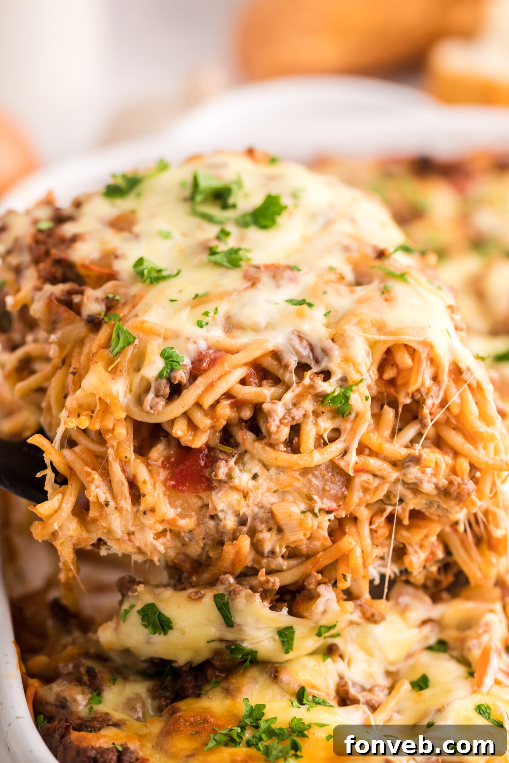 A generous slice of Million Dollar Spaghetti Casserole being lifted from the baking pan with a spatula, showcasing its distinct layers of pasta, meat sauce, and creamy cheese