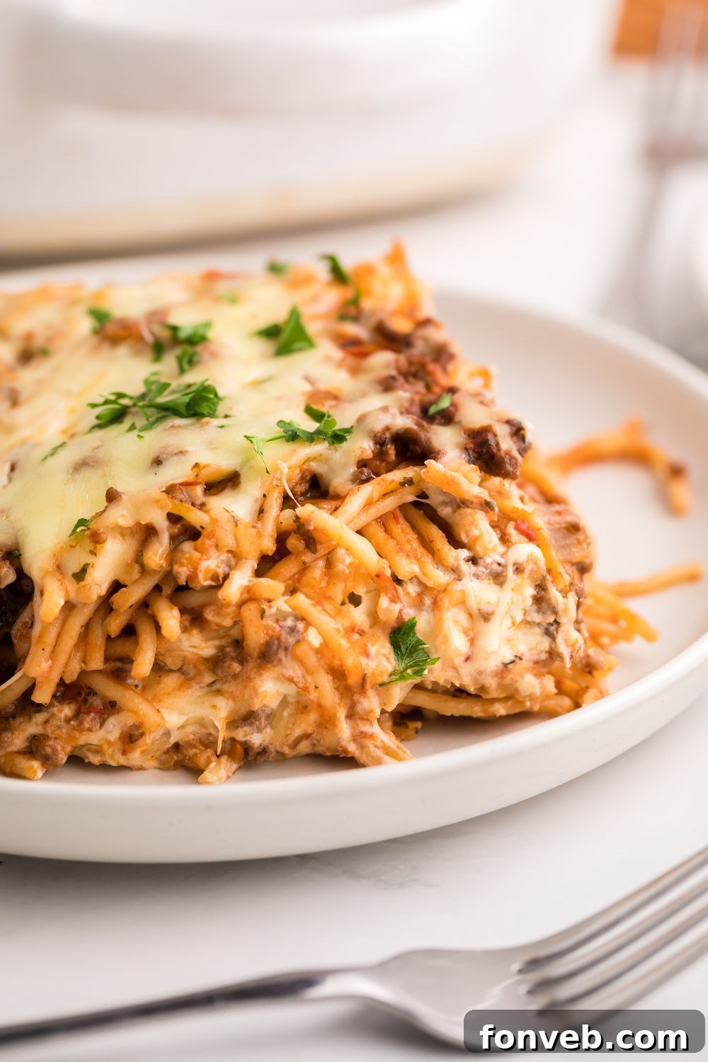 Close-up of a generous slice of Million Dollar Spaghetti Casserole on a white plate, revealing the intricate layers