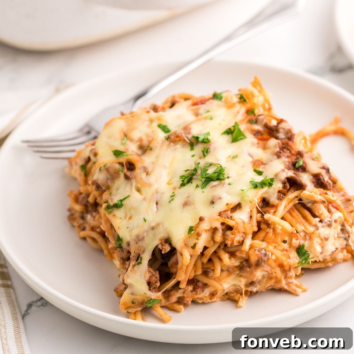 Million Dollar Spaghetti Casserole on a plate with a fork on the side, showcasing a delicious bite
