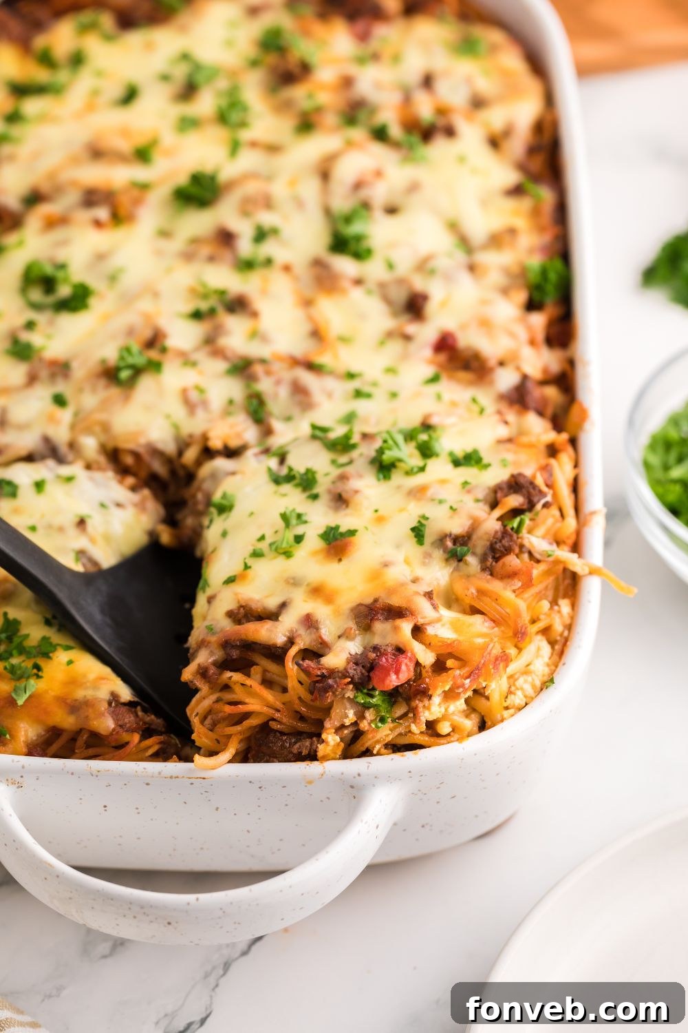 Scooping a generous portion of Million Dollar Spaghetti Casserole from the pan with a spatula, showing the rich, cheesy layers