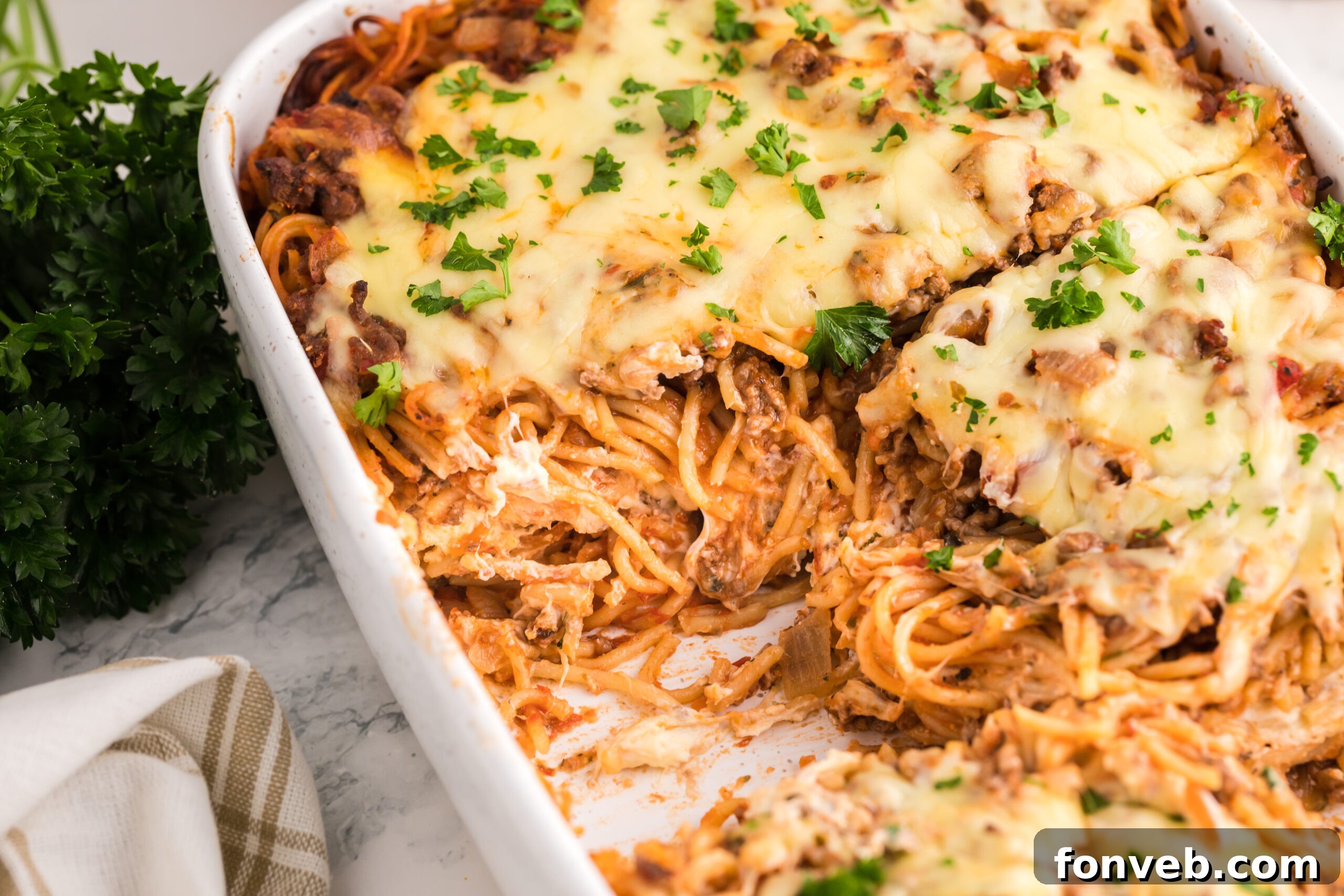 Million Dollar Spaghetti Casserole in a white baking dish with a couple slices removed, showing its golden, bubbly crust and inviting interior