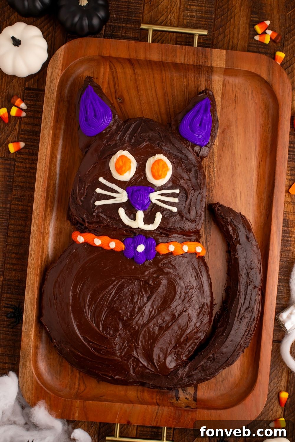 Purrfectly Simple 4-Ingredient Black Cat Halloween Cake 14 Easy Halloween Black Cat Cut Out Cake on a tray with fake pumpkins around the tray and candy corn candy to side, enhancing the festive display