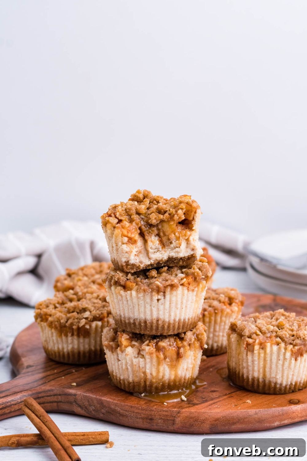wooden cutting board sitting on marble counter with a towel behind it on table. On the tray is stacks of Apple Crisp Cheesecake Bites with one of the cheesecakes with some bites taken out of it 