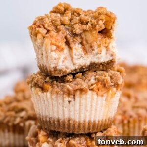 Mini Apple Crisp Cheesecakes stacked on top of one another on table with more spread out behind it on table