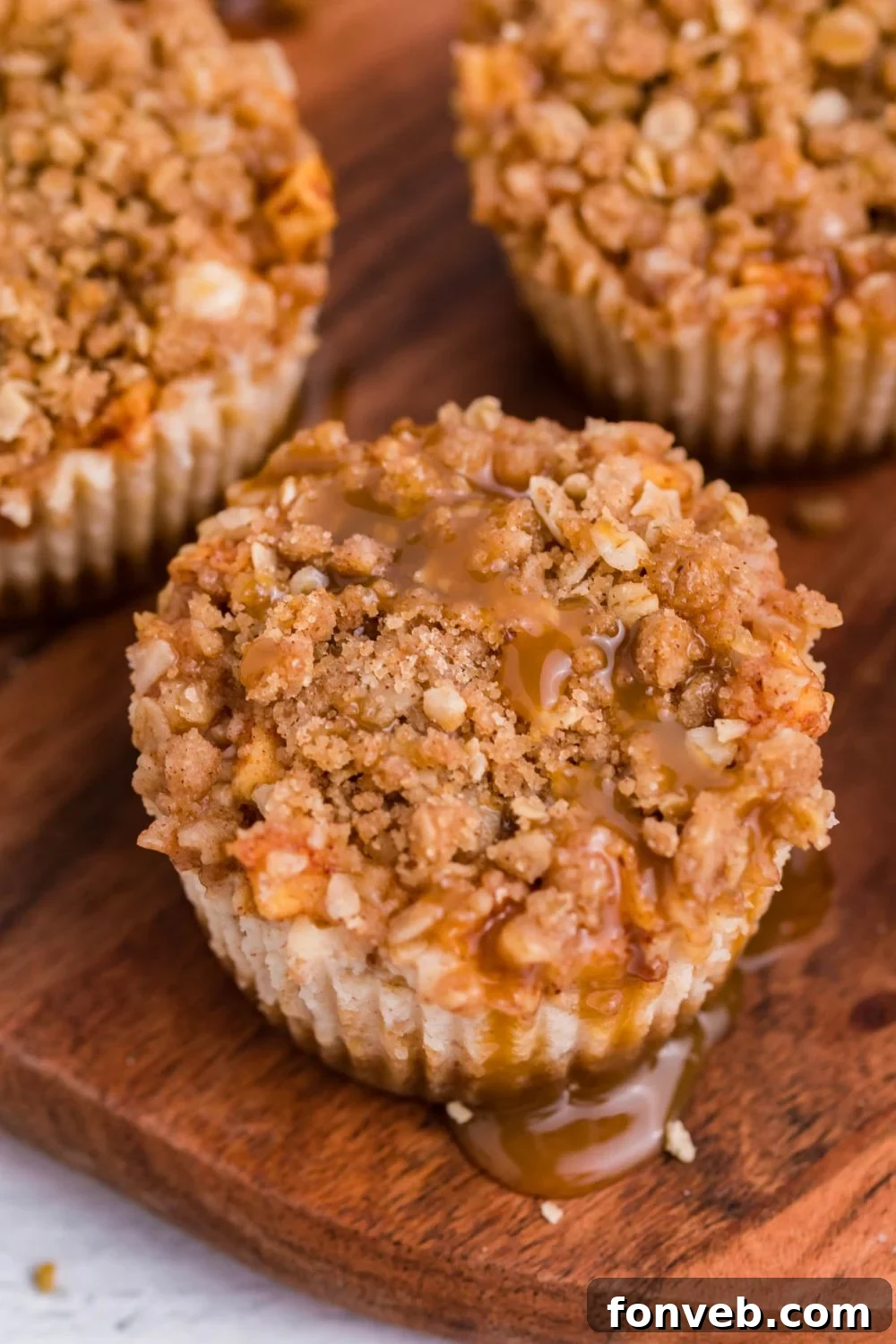 white table with wooden cutting board on top with Apple Crisp Cheesecake Bites on top drizzled with caramel sauce