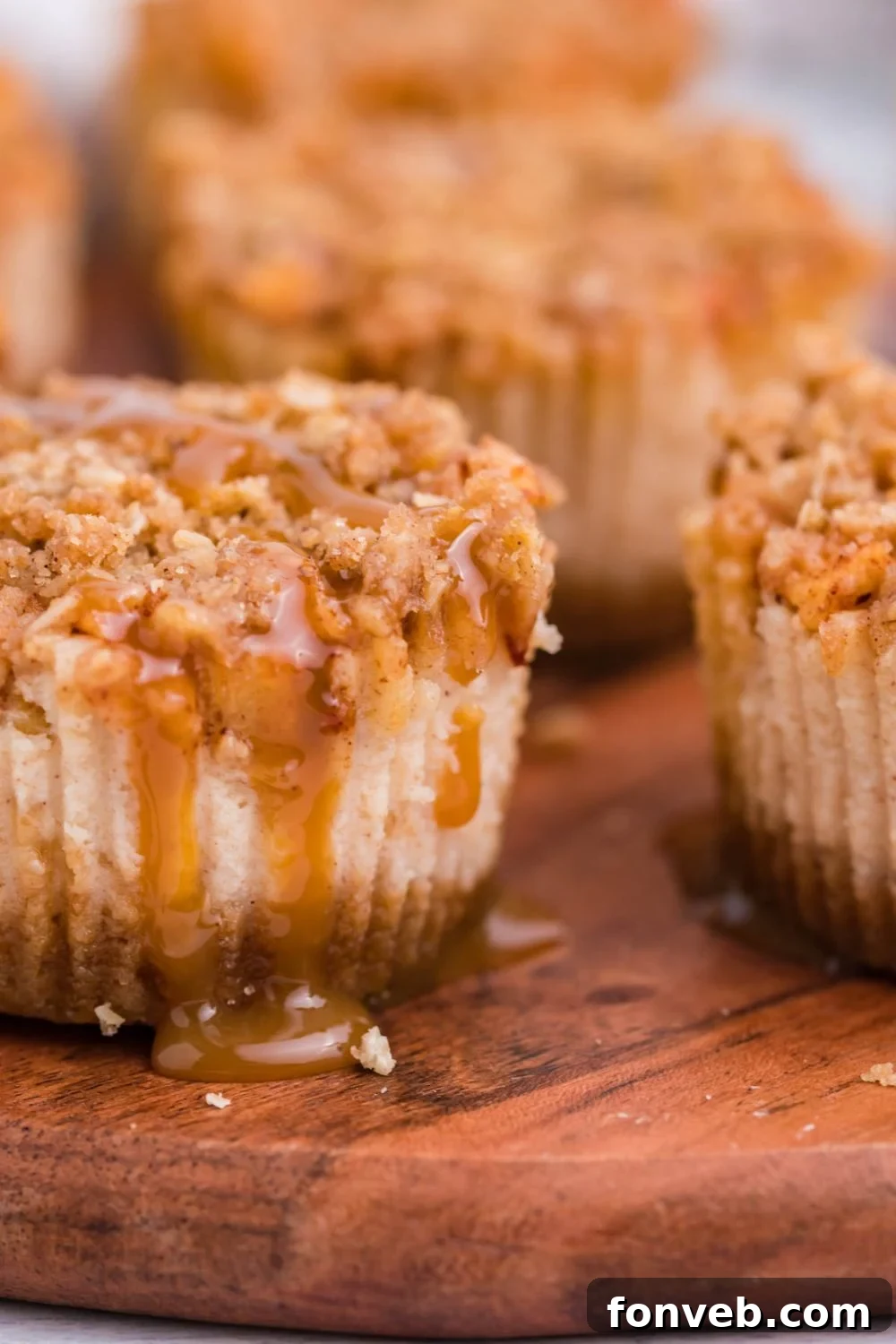 Apple Crisp Cheesecake Bites with caramel sauce drizzled down the sides. The cheesecakes are placed on a wooden table sitting on a white table
