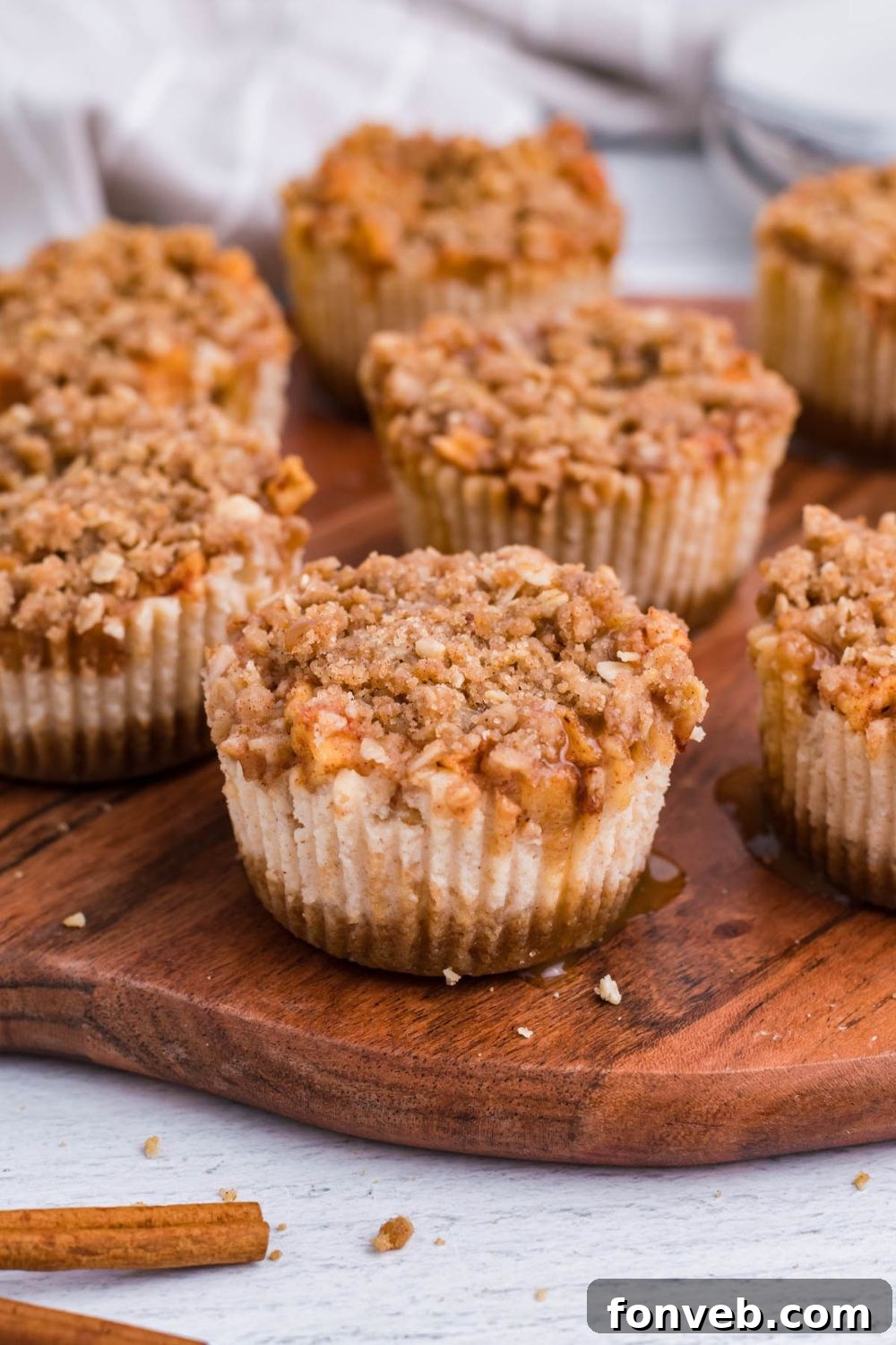 marble counter with around wooden cutting board with Apple Crisp Cheesecake Bites placed all over board with some drizzle of caramel all over the cheesecakes