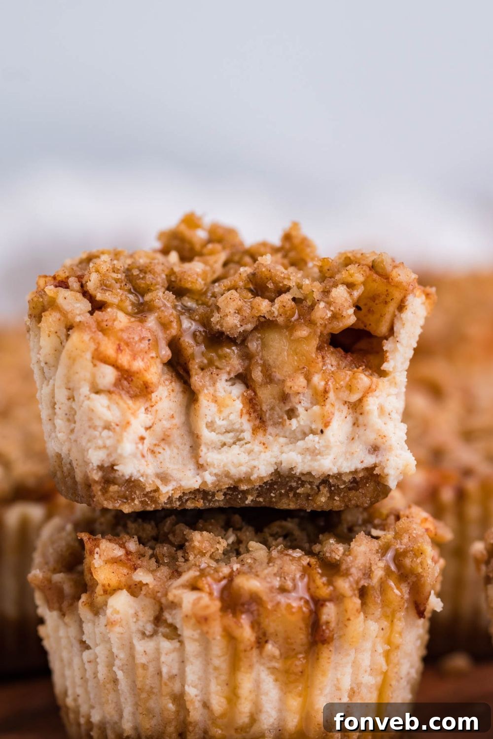 two Apple Crisp Cheesecake Bites stacked on top of each other on wooden cutting board. The top cheesecake has a few bites taken out of it 
