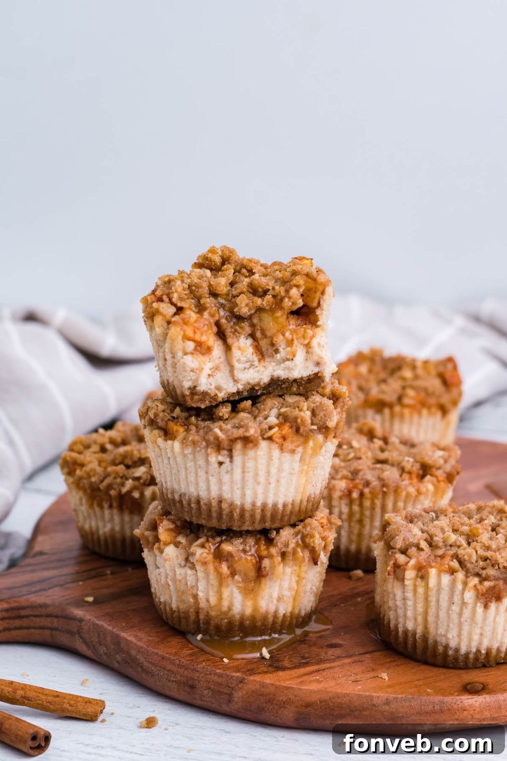 marble counter with a round cutting board on it, with stacks of Apple Crisp Cheesecake Bites. There are cinnamon sticks to side on table 