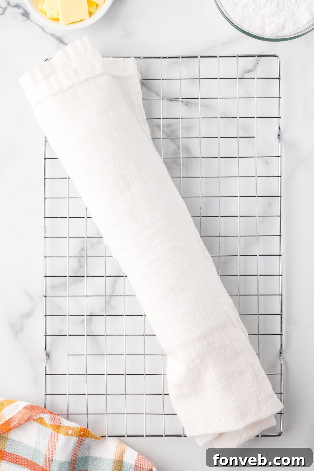 Classic Spiced Pumpkin Roll 13 Pumpkin Cake Roll wrapped up in a white towel on a cooling rack on a marble counter