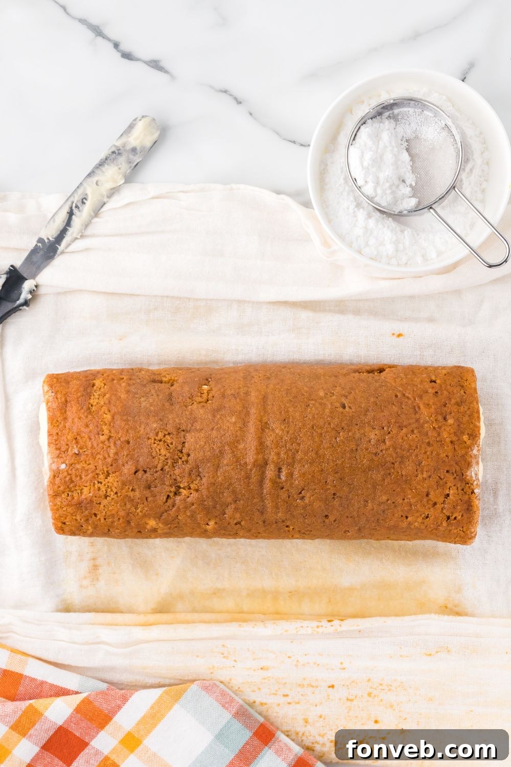 Classic Spiced Pumpkin Roll 16 Pumpkin Cake Roll being rolled up with parchment paper under the pumpkin cake
