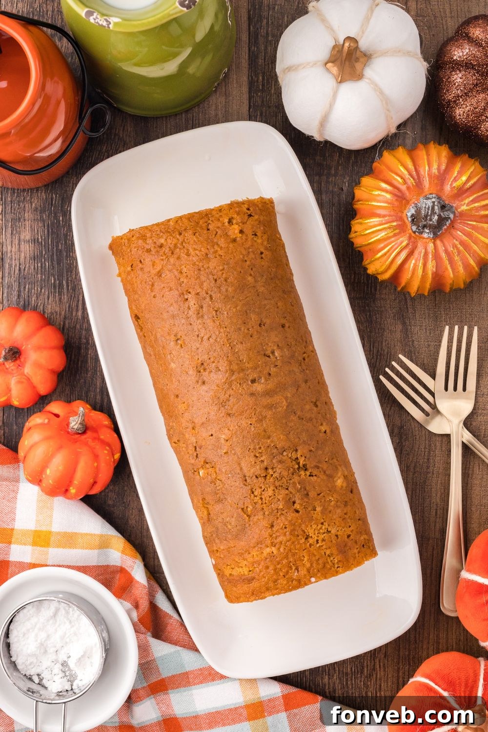 Classic Spiced Pumpkin Roll 17 Pumpkin Cake Roll sitting on a long platter with faux pumpkins to side and forks on side