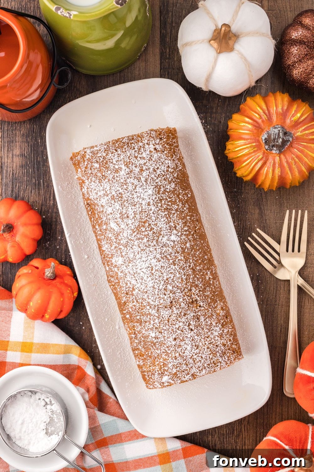Classic Spiced Pumpkin Roll 18 Pumpkin Cake Roll on a long platter sitting on a rustic wooden table with forks to side