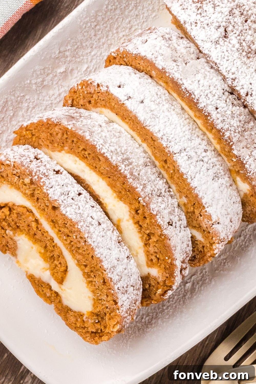 Classic Spiced Pumpkin Roll 19 sliced Pumpkin Cake Roll on a tray sitting on a wooden table with a fork to the side