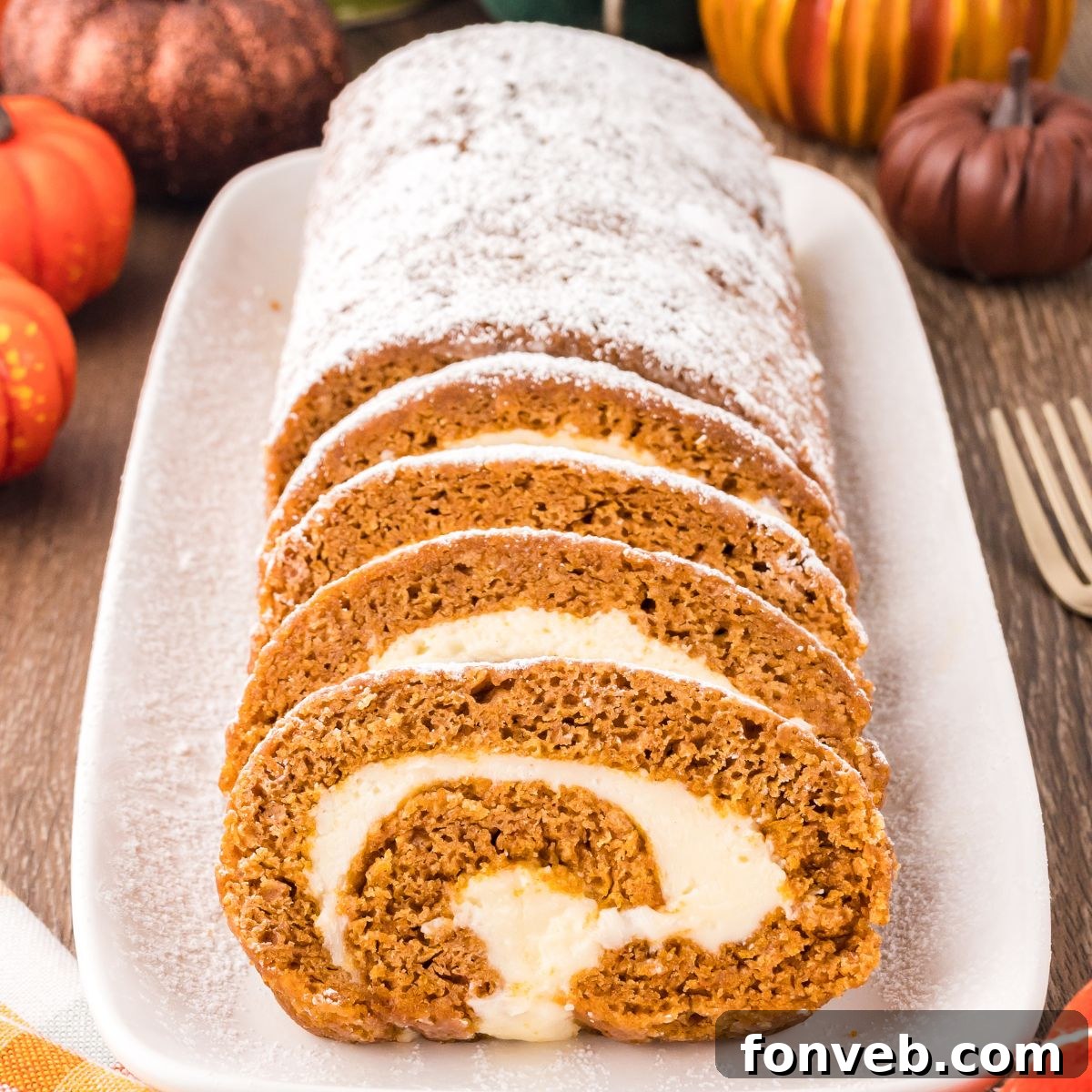 Classic Spiced Pumpkin Roll 3 Pumpkin Roll on a long platter sitting on wooden table with pumpkins around to set a fall theme. Part of the pumpkin roll is sliced and the other part is not sliced and dusted with powdered sugar