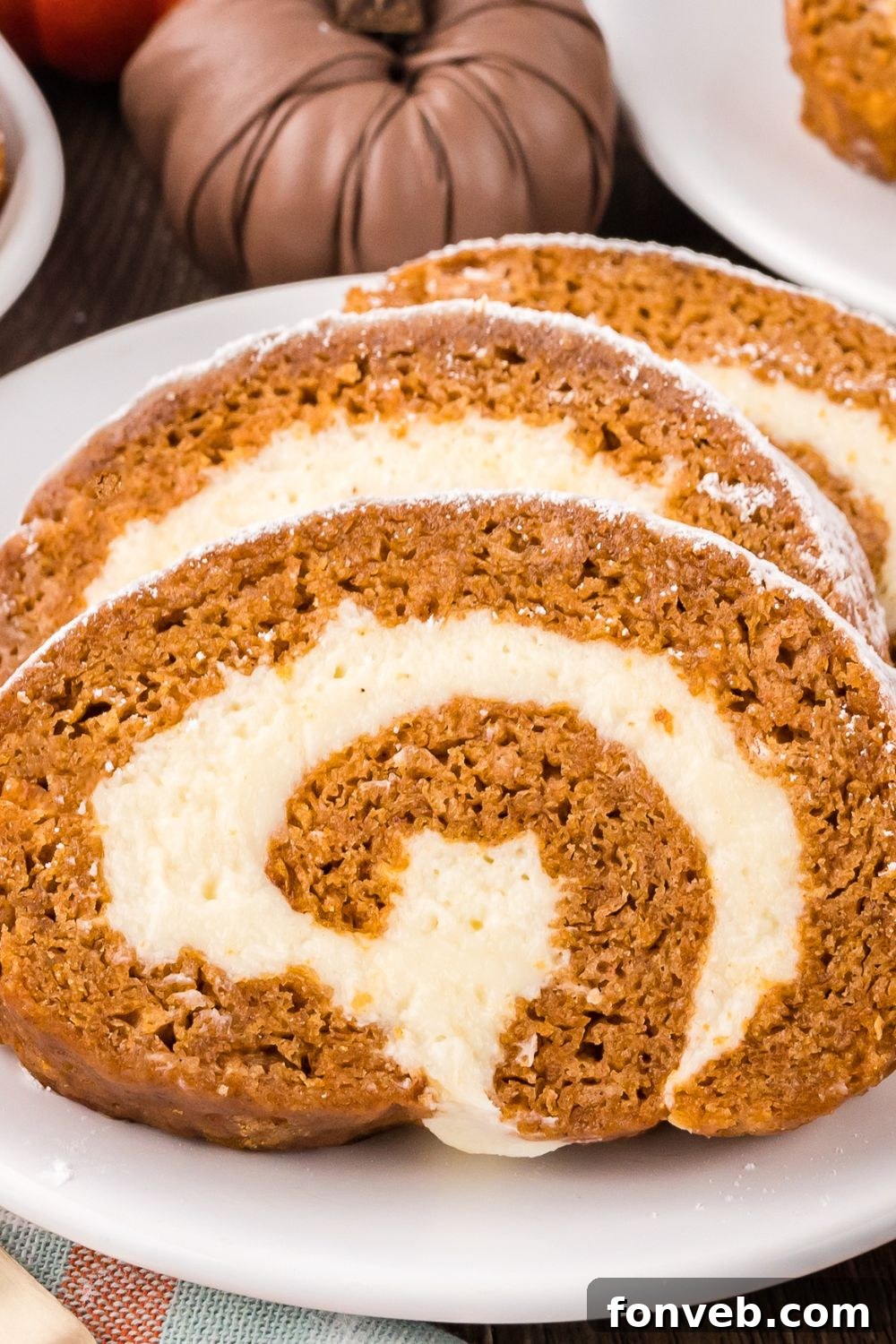 Classic Spiced Pumpkin Roll 24 a white plate on table with three thick slices of Pumpkin Cake Roll on it, and mini pumpkins to side of plate