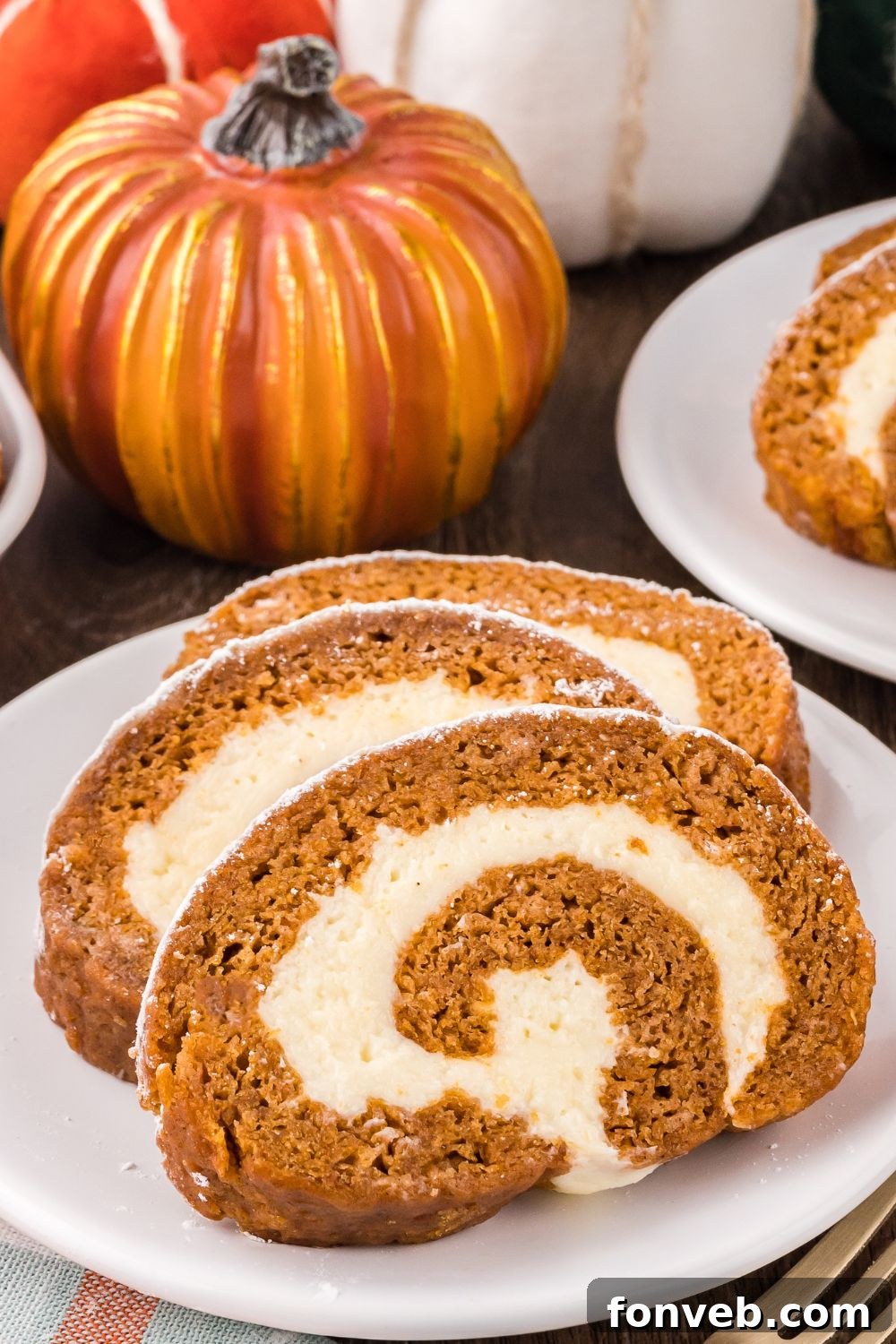 Classic Spiced Pumpkin Roll 27 Pumpkin Cake Roll sliced on white plates placed on table with a few faux pumpkins around the plates to give a fall theme to table
