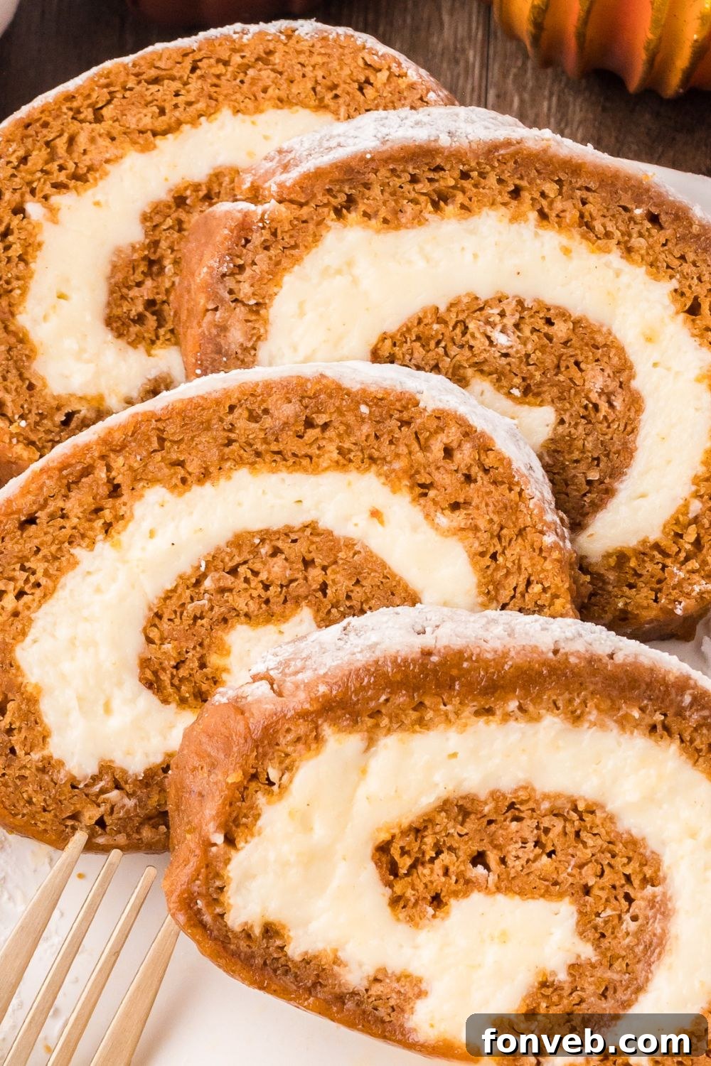 Classic Spiced Pumpkin Roll 29 thick slices of Pumpkin Cake Roll on a white plate with a fork sitting in front of the plate that is sitting on a wooden table
