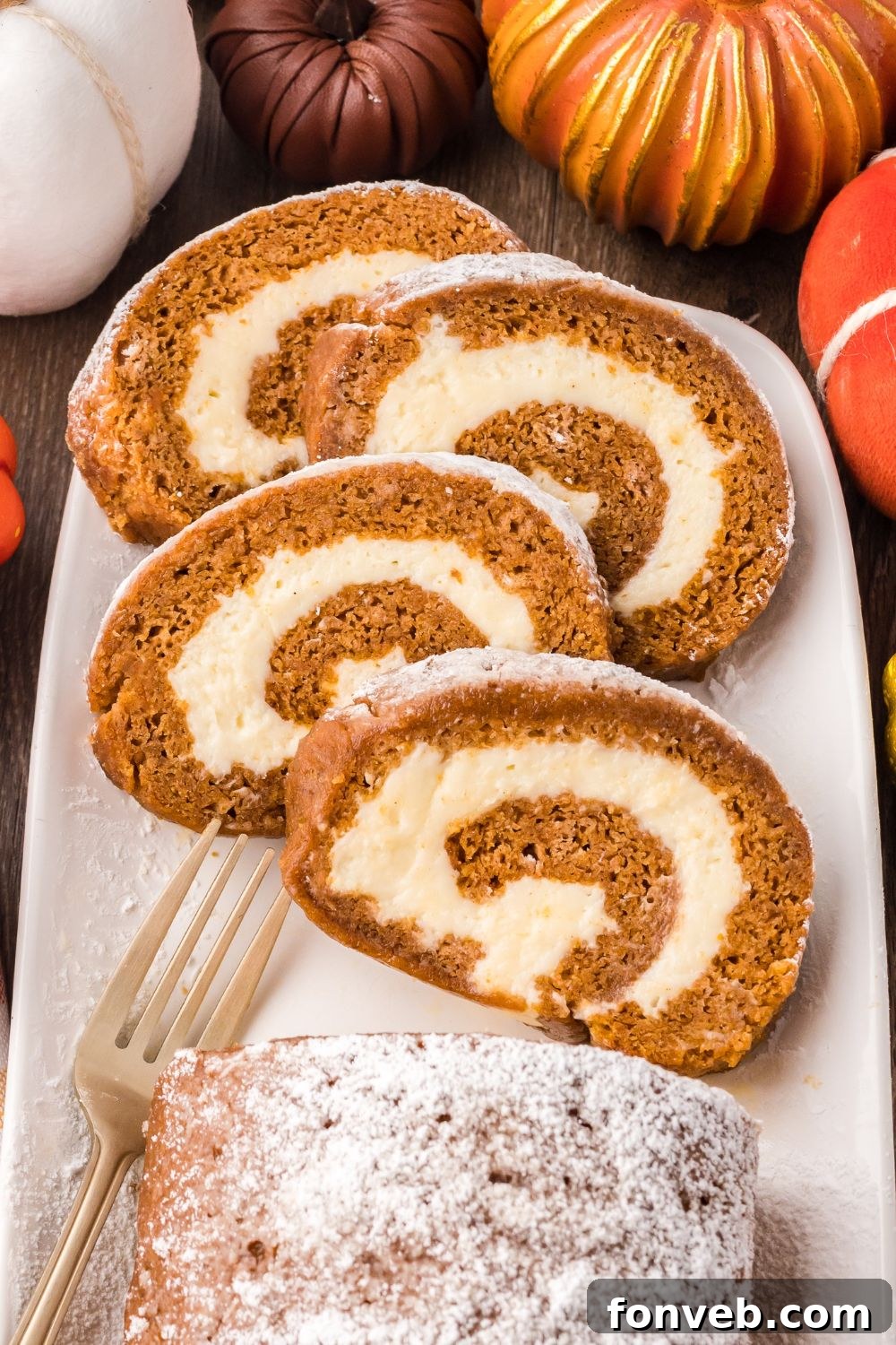 Classic Spiced Pumpkin Roll 4 Pumpkin Cake Roll sliced and placed on a platter, and faux pumpkins around the platter for a fall themed rustic look