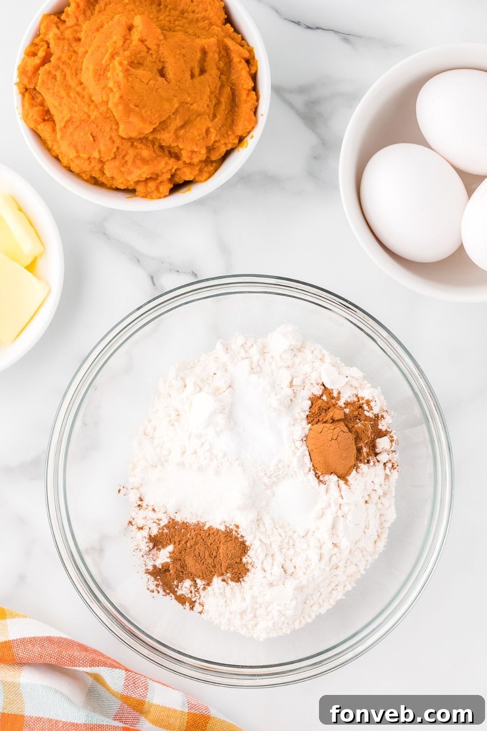 Classic Spiced Pumpkin Roll 7 flour, spices and more in a glass bowl with small bowls around it with eggs, pumpkin and sliced butter for making Pumpkin Cake Roll