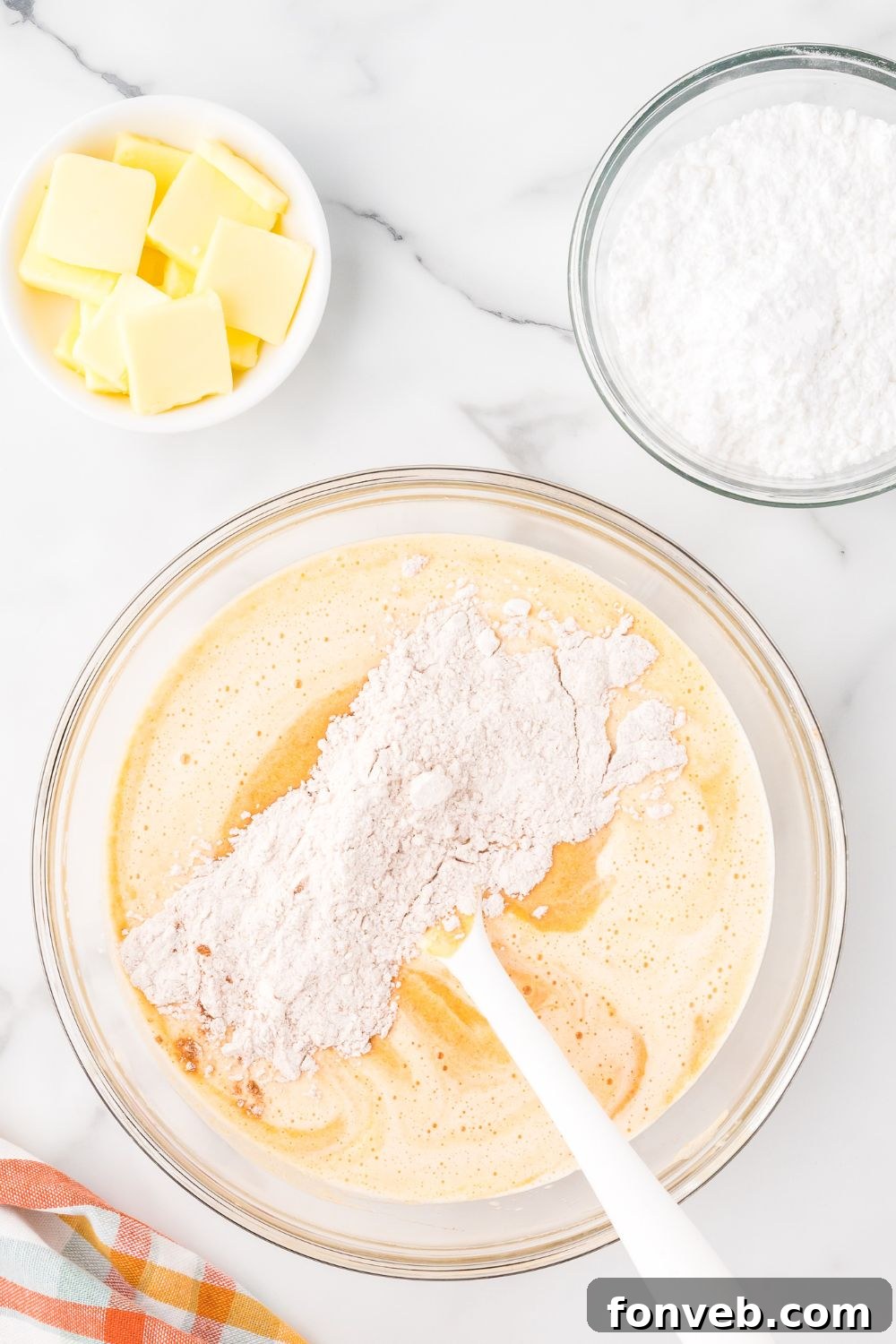Classic Spiced Pumpkin Roll 9 mixing up Pumpkin Cake Roll batter in a glass bowl on marble counter with butter and powdered sugar in smaller bowls to the side