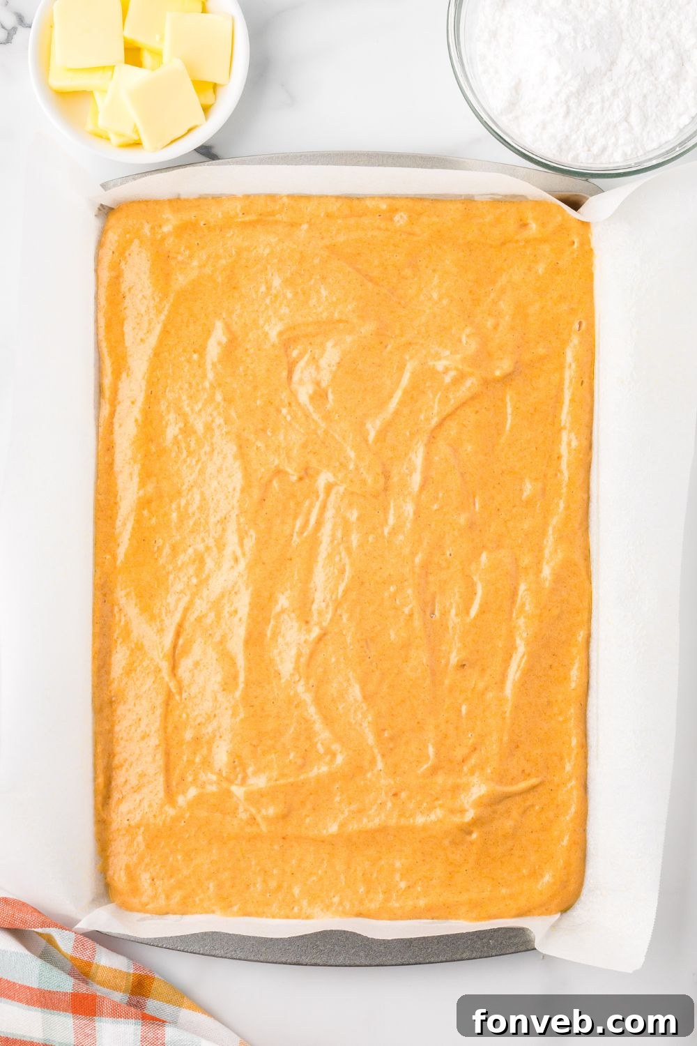 Classic Spiced Pumpkin Roll 10 Pumpkin Cake Roll batter spread out in a baking pan sitting on table with parchment paper under it