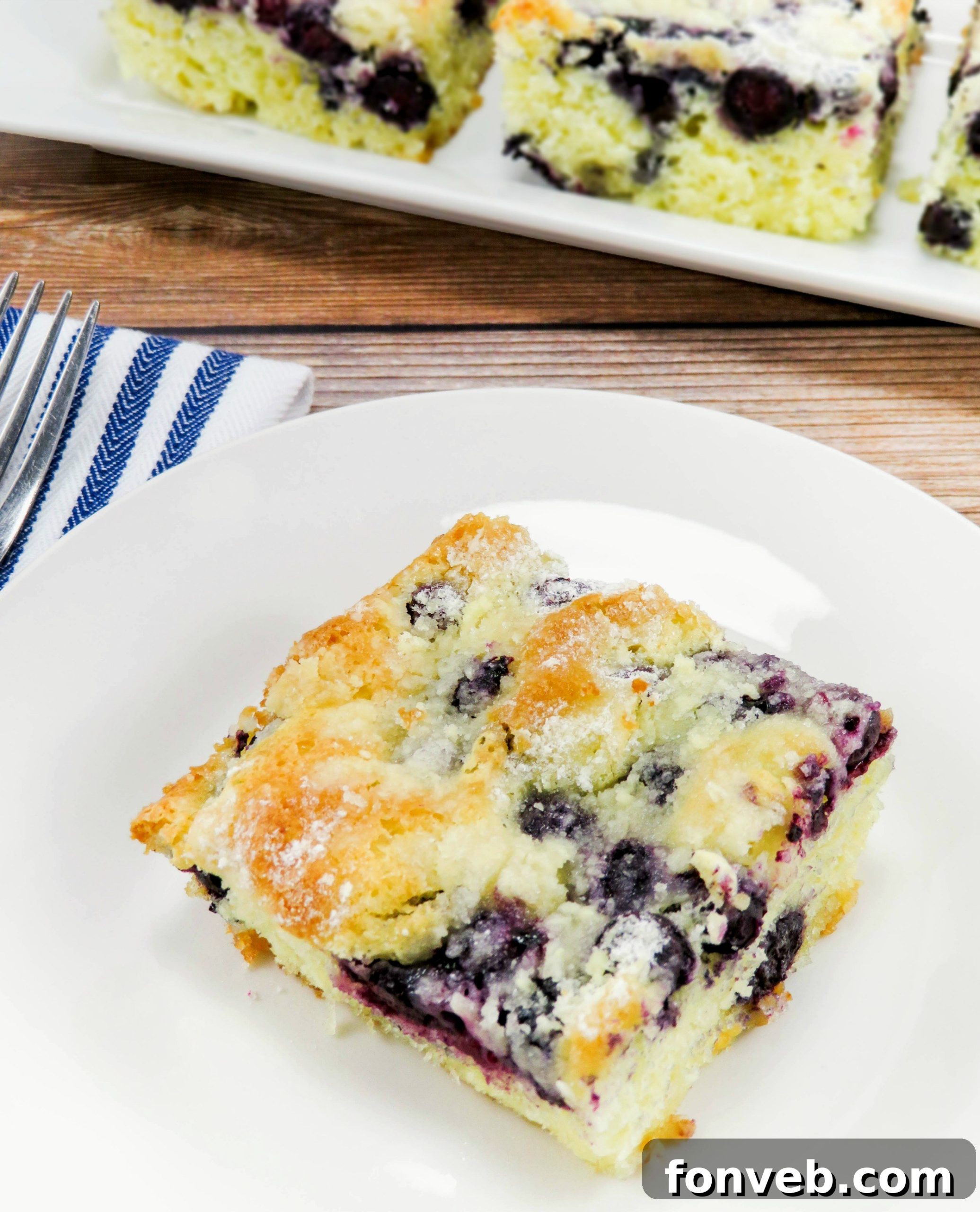 A slice of blueberry butter cake served on a plate, showing the rich, moist interior and abundance of blueberries