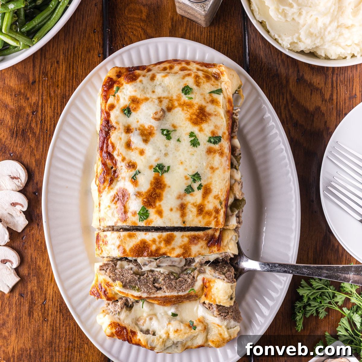 Stuffed Philly Cheesesteak Meatloaf on a white platter on wooden table that is partly sliced and ready to serve 