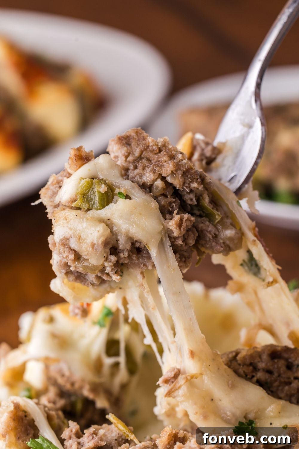 fork with a bunch of cheesy Stuffed Philly Cheesesteak Meatloaf being lifted up off a plate full of more meatloaf sitting on wooden table 