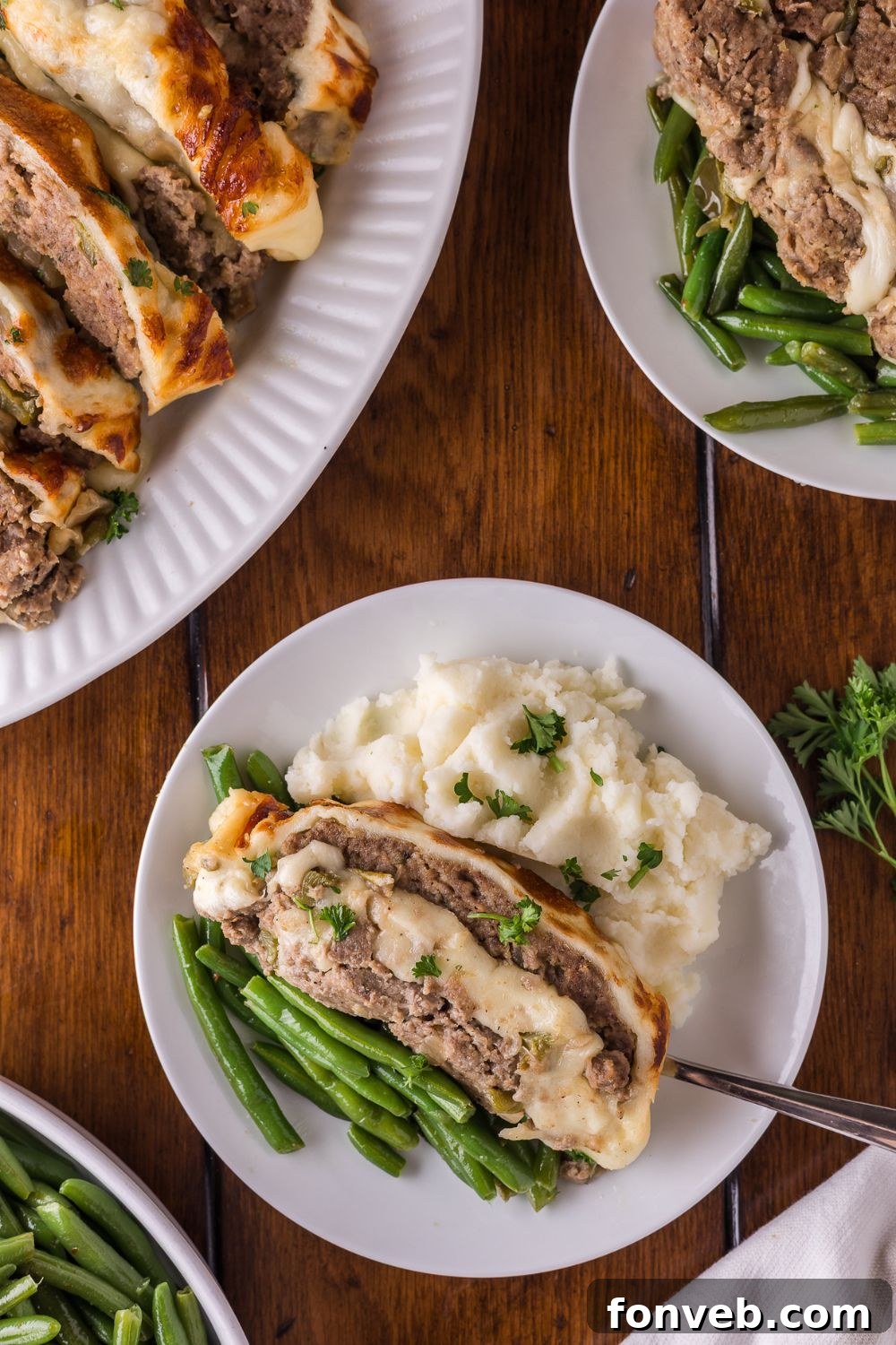 a dinner table with a platter full of sliced Stuffed Philly Cheesesteak Meatloaf, and plates that have meatloaf, mashed potatoes and green beans on it 