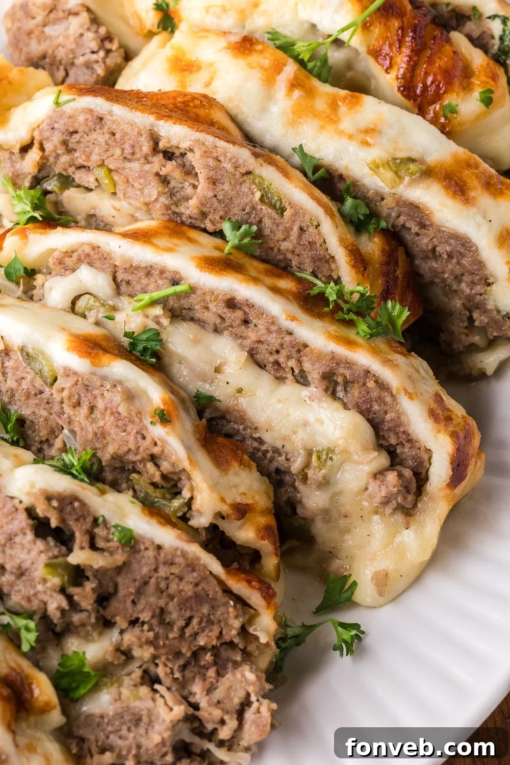 sliced Stuffed Philly Cheesesteak Meatloaf on a white platter that is sprinkled with parsley on top of meatloaf