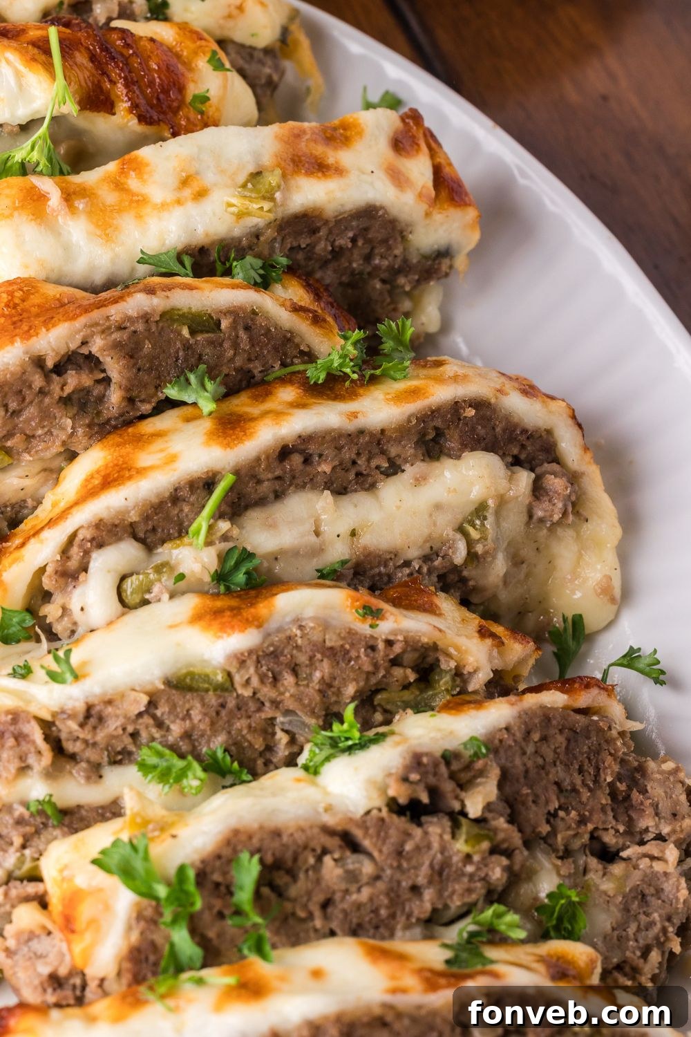 a white plate on wooden table with sliced Stuffed Philly Cheesesteak Meatloaf on plate topped with chopped parsley